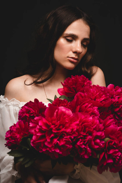 retrato de una joven sensual con un ramo de peonías rojas en sus manos - Foto, imagen