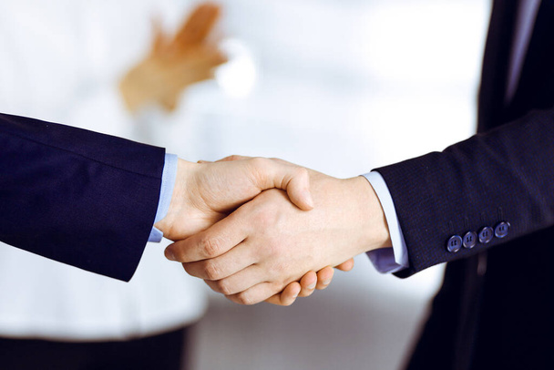 Business people shaking hands at meeting or negotiation, close-up. Group of unknown businessmen and a woman standing in a modern office. Teamwork, partnership and handshake concept - Photo, image