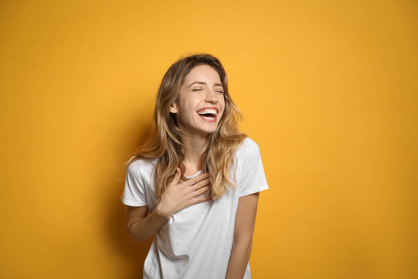 Cheerful young woman laughing on yellow background - Фото, изображение