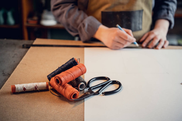 A primeira etapa na produção de sapatos é fazer um padrão exato de papel, um jovem sapateiro de uniforme no trabalho. Instrução 1 - Foto, Imagem