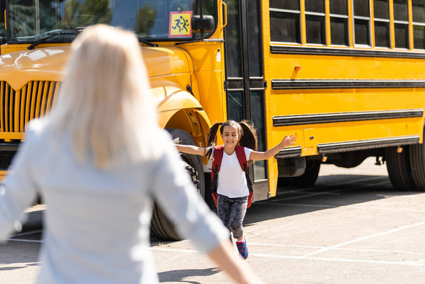 Dzieciaki wpadają w ręce matek, żeby ją uściskać po powrocie do szkoły w pobliżu szkolnego autobusu. - Zdjęcie, obraz