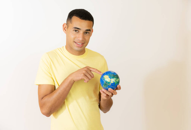 Jeune homme tenant un globe sur un fond blanc - Photo, image