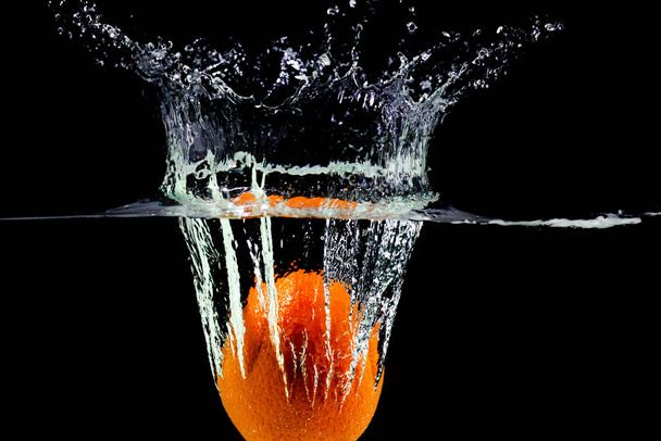 fruit orange falls into the water with splashes on a black background - Foto, imagen