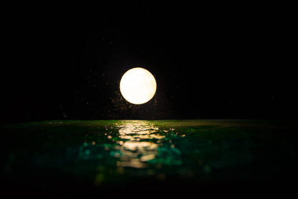 Romantic and scenic panorama with full moon on sea to night. Table decoration with moon miniature and water. Selective focus - Valokuva, kuva