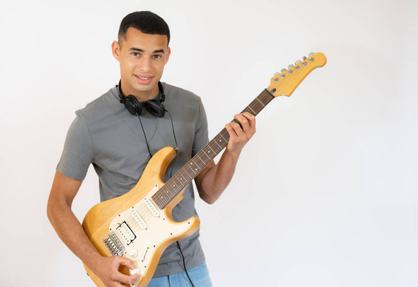 Όμορφος νεαρός άνδρας που παίζει ηλεκτρική κιθάρα απομονωμένος σε λευκό φόντο. - Φωτογραφία, εικόνα