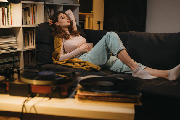 жінка розслабляється на дивані вдома під час прослуховування записів на грамофон
 - Фото, зображення