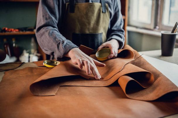 Experienced specialist in the production of footwear leather lays on a table in his workshop - Photo, Image