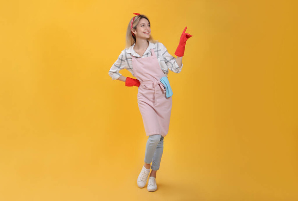 Young housewife in gloves on yellow background - Foto, Bild