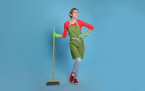 Young housewife with broom on light blue background - Foto, Bild