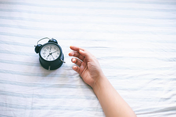 Time optimization concept. Female hand holding alarm clock on bed background, close up view - Fotó, kép