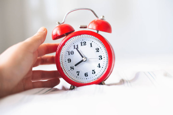 Concepto de optimización temporal. Reloj despertador de mano femenino en el fondo de la cama, vista de cerca - Foto, Imagen