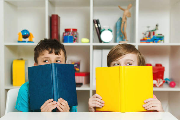 Two school boys hiding behind books at classroom. Happy friends having fun together after lesson. Education and development. Back to school concept. School children holding books. - Zdjęcie, obraz
