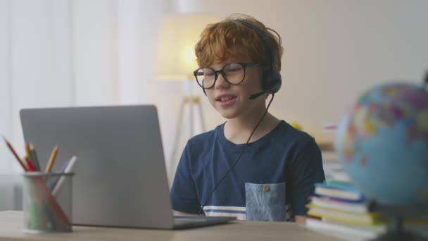 Petit garçon rousse portant un casque avec micro vidéo bavarder avec tuteur, regarder un ordinateur portable et parler à l'enseignant - Séquence, vidéo