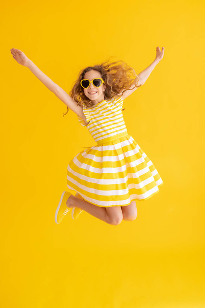 Happy child jumping against yellow summer background. Portrait of cheerful girl. Success and winner concept - Valokuva, kuva
