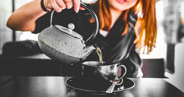 woman hand with metal teapot pour black tea in black glass cup in cafe - Фото, зображення