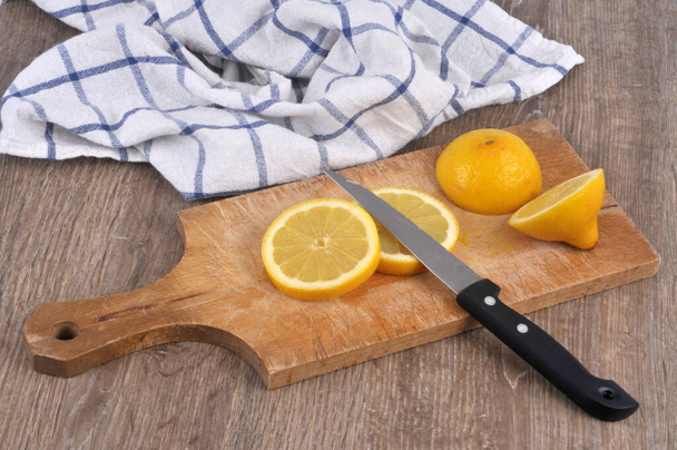Sitruuna leikataan viipaleiksi leikkuulaudalla veitsellä lähikuva puinen tausta  - Valokuva, kuva