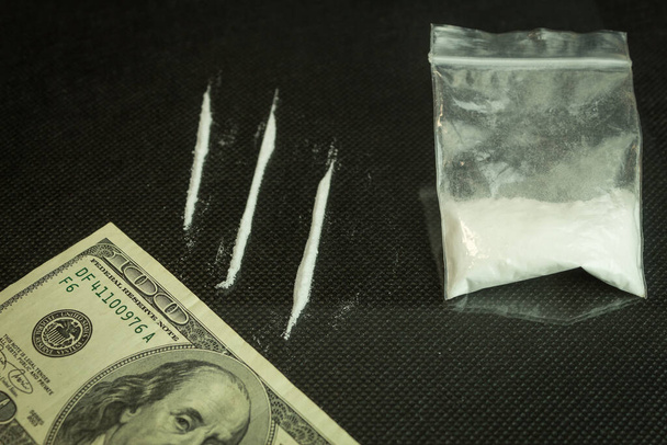Drogy a dolary na sklo, černý stůl. Narkotický prášek rozdělený na pruhy na zrcadlovém stole, 100dolarová tuba pro užívání drog - Fotografie, Obrázek