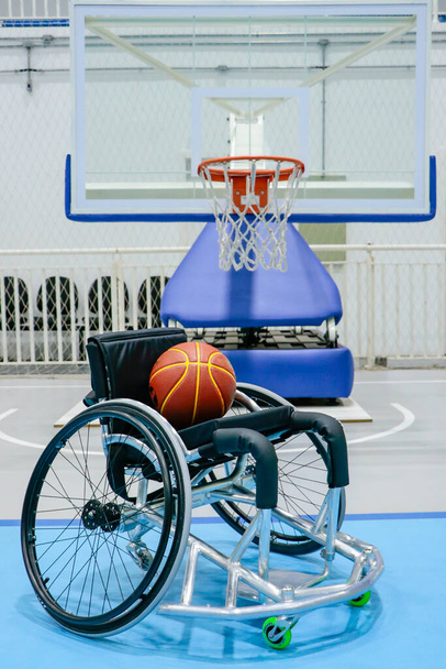 Rolstoel voor verlammende basketbalspelers, met een wedstrijdbal op de stoel en onderaan de tafel met de basketbalring - Foto, afbeelding