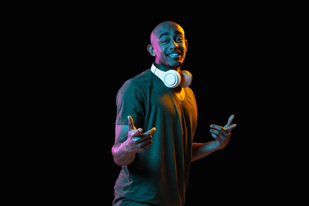 African-american young mans portrait on dark studio background in neon. Concept of human emotions, facial expression, youth, sales, ad. - Φωτογραφία, εικόνα