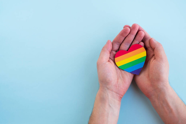 Corazón de arco iris LGBT en las manos del hombre. Mes de orgullo, amor y concepto de tolerancia. Vista superior, espacio de copia - Foto, imagen