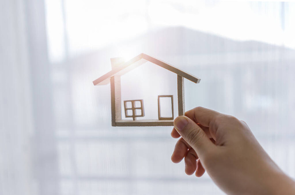 Mão-segurando casa modelo em miniatura com ataques de luz solar. Conceito de compra de imóveis e casa nova. - Foto, Imagem