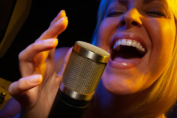 Female vocalist under gelled lighting sings with passion into condenser microphone. - Fotoğraf, Görsel