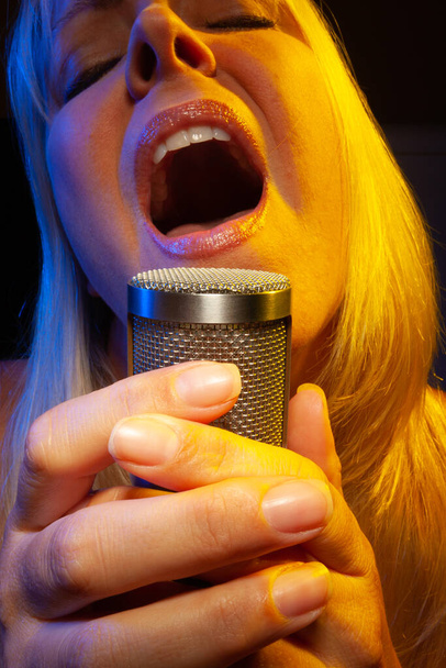 Sängerin singt unter geliertem Licht leidenschaftlich in Kondensatormikrofon. - Foto, Bild