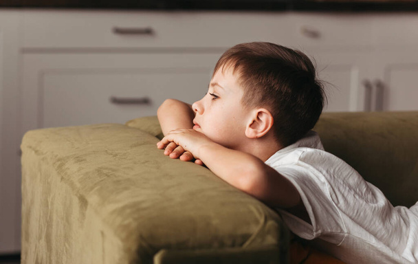 Egy iskolás fiú unatkozik otthon, a kanapén fekve, társadalmi távolságban, karanténban, elszigetelten. lezárási koncepció. mentális egészség - Fotó, kép