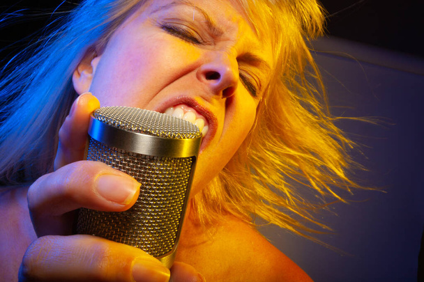 Female vocalist under gelled lighting sings with passion into condenser microphone. - Photo, Image