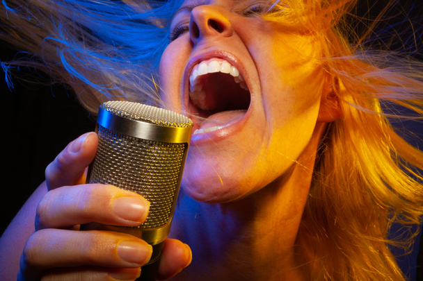 Female vocalist under gelled lighting sings with passion into condenser microphone. - Фото, изображение