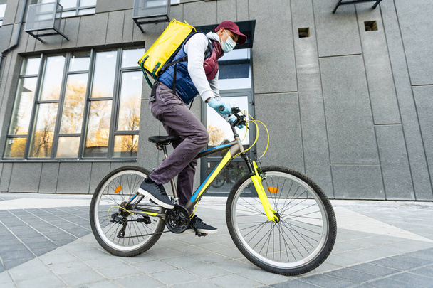 Delivery Man standing with yellow thermo backpack for food delivery near the entrance home with empty space to copy paste - Fotoğraf, Görsel