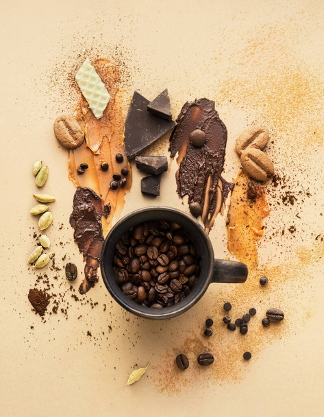 Creative coffee background for coffee shop. Cup with coffee beans, smeared on the background with caramel and chocolate with spices. Copy space. - Photo, image