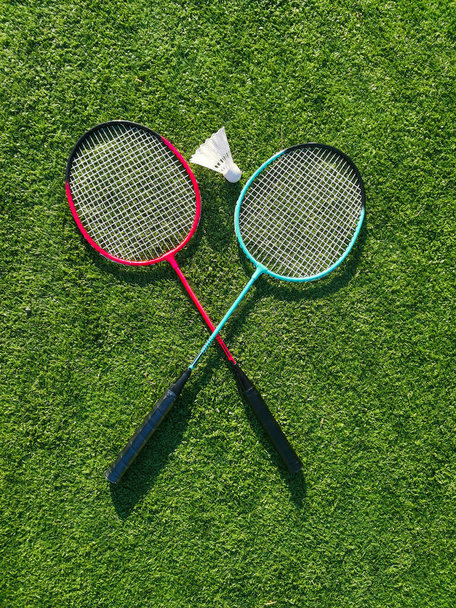 Rode badminton rackets en shuttlecock liggen op het kunstgras van een sportstadion. Een amateurbadmintonset. Concept van de zomer hobby, buitensporten, entertainment. Plaats voor tekst, platte lay. - Foto, afbeelding