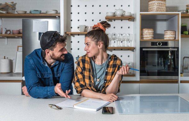 Young happy couple standing in their kitchen and want to make a list of people and friends who they will invite to their wedding ceremony - Foto, Imagen