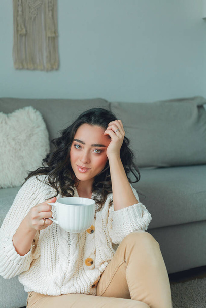 Beautiful young dark-haired curly woman is drinking tea at home. Quarantine. Cafe. - Fotoğraf, Görsel