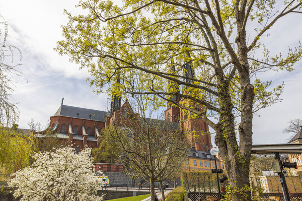 Schöne Aussicht auf die Kathedrale von Uppsala durch Frühlingsbäume am bewölkten Himmel Hintergrund. Schweden. - Foto, Bild