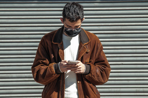 young man with mask and mobile phone on the street - Foto, Imagen
