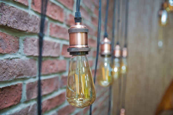 Edison lambasının arka planındaki tuğla duvar. Arka planda bokeh efektli klasik elektrik ampulü ile iç aydınlatma dekorasyonu - Fotoğraf, Görsel