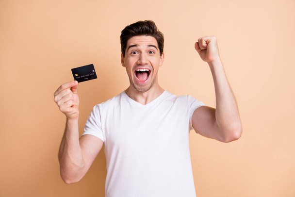 Portrait of delighted handsome guy fist up open mouth celebrate hold debit card isolated on beige color background - Foto, afbeelding
