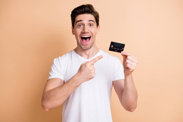 Photo of astonished guy open mouth direct finger debit card unexpected promo isolated on beige color background - Fotó, kép