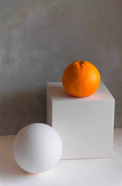 Minimalistický koncept zátiší s hroznovým ovocem a sklenicí grapefruitové šťávy na bílé geometrické kostce postava na bílém stole a šedém pozadí, vertikální, kopírovací prostor, abstraktní design moderního umění - Fotografie, Obrázek