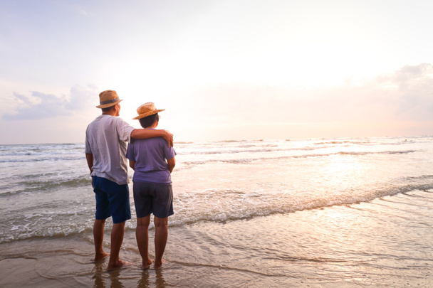Ein älteres asiatisches Paar steht morgens gemeinsam am Strand und blickt auf das schöne Meer. Reisekonzept für ein glückliches Leben im Rentenalter. Kopierraum - Foto, Bild