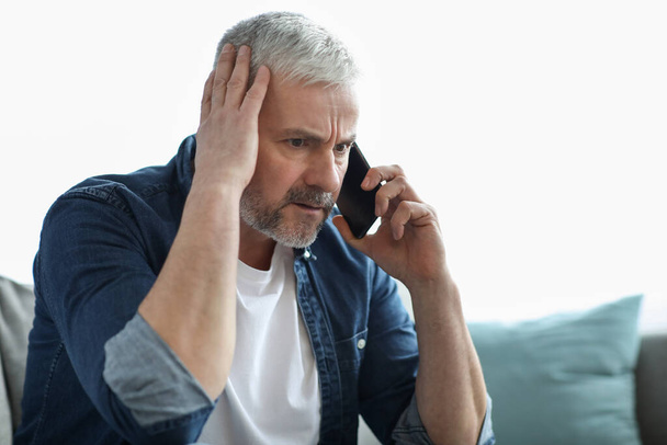Hombre mayor preocupado teniendo conversación telefónica, tocándose la cabeza - Foto, Imagen