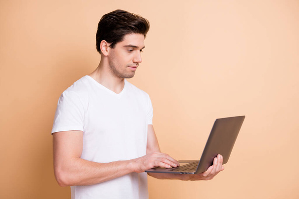 Profile portrait of optimistic brunet man type laptop wear white t-shirt isolated on beige color background - Foto, afbeelding