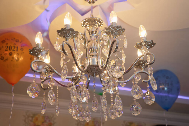 Luxuriöser Kronleuchter mit Kerzen im Inneren. An der Decke hängt ein edler Leuchter mit vielen kleinen Perlen. Eine hochwertige Dekoration für eine Palast-Gala, ein Geschäftstreffen in einer Villa oder eine Hochzeit. - Foto, Bild