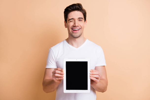 Portrait of funny friendly man arms hold tablet showing display eye wink isolated on beige color background - Φωτογραφία, εικόνα