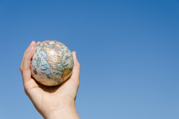 глобальная земная игрушка в руке на фоне голубого неба
   - Фото, изображение