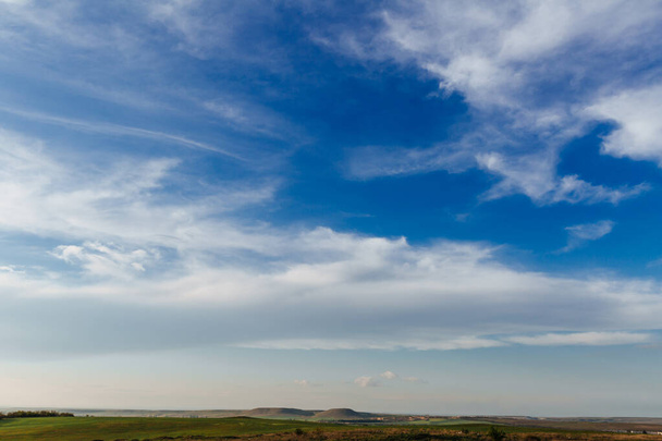 Белые облака простирались по синему небу в теплый солнечный день, а под небом были зеленые поля и холмы - Фото, изображение