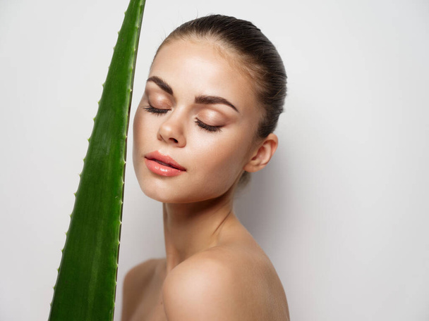 woman with closed eyes and green aloe leaf on light background cropped view - Zdjęcie, obraz