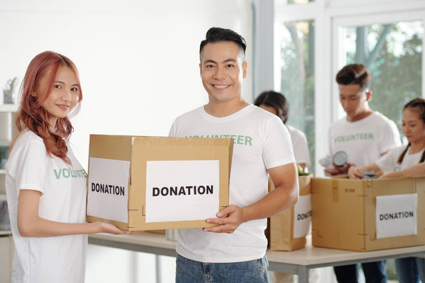 Νεαρό ζευγάρι Ασιατών που εργάζονται ως εθελοντές στο κέντρο αιμοδοσίας, συσκευάζουν κουτιά για ανθρώπους που έχουν ανάγκη - Φωτογραφία, εικόνα
